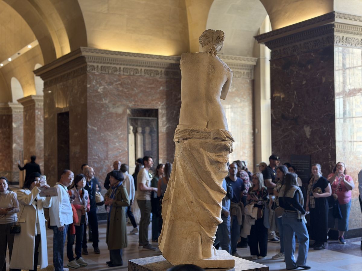 The Venus de Milo at the Louvre seen from behind, with visitors around the statue